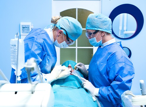 Two dentists performing implant surgery in blue scrubs