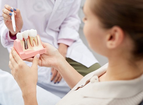 Dentist pointing to sample dental implant held by patient