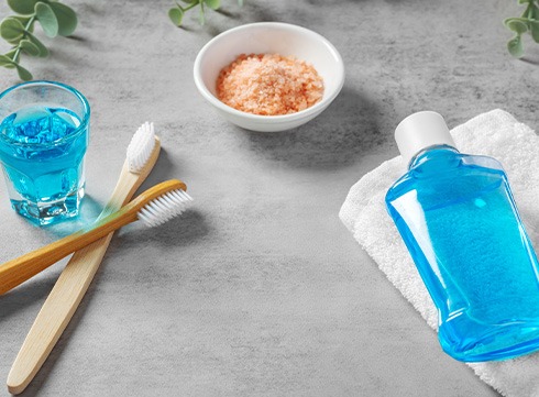 Wooden toothbrushes next to bottle of mouthwash and small bowl of salt