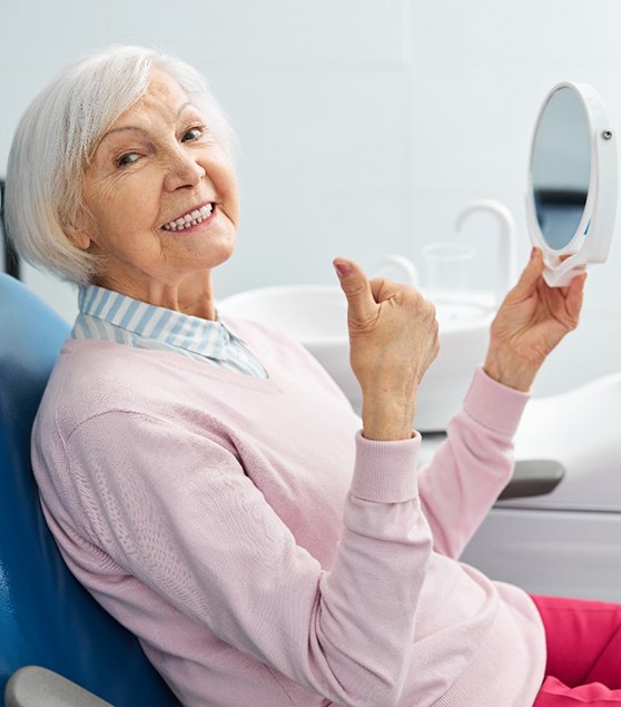 Senior woman smiling and giving thumbs up while holding mirror