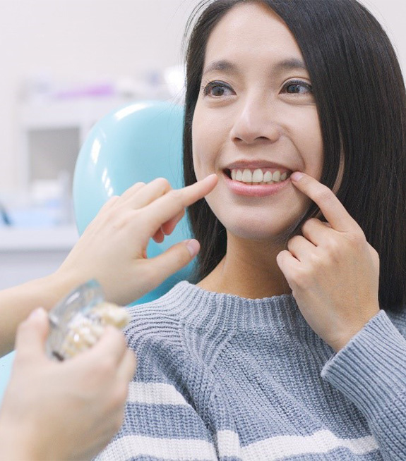 Woman in dental chair pointing to her smile